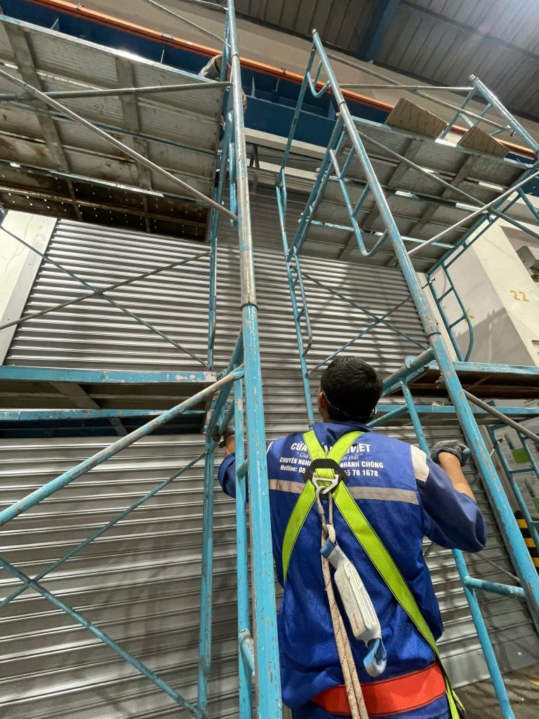 Thợ lắp cửa cuốn kho xưởng trên giàn giáo